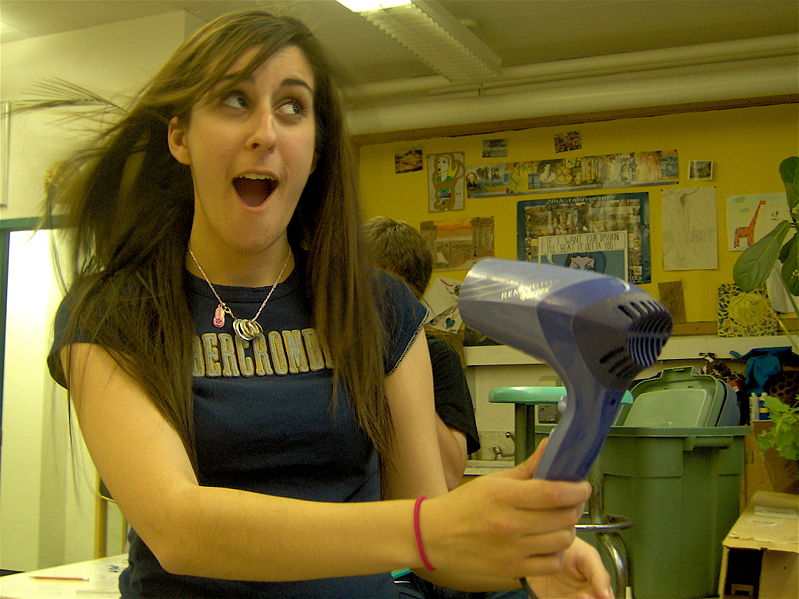 Long-haired woman posing with a blowing hairdryer.