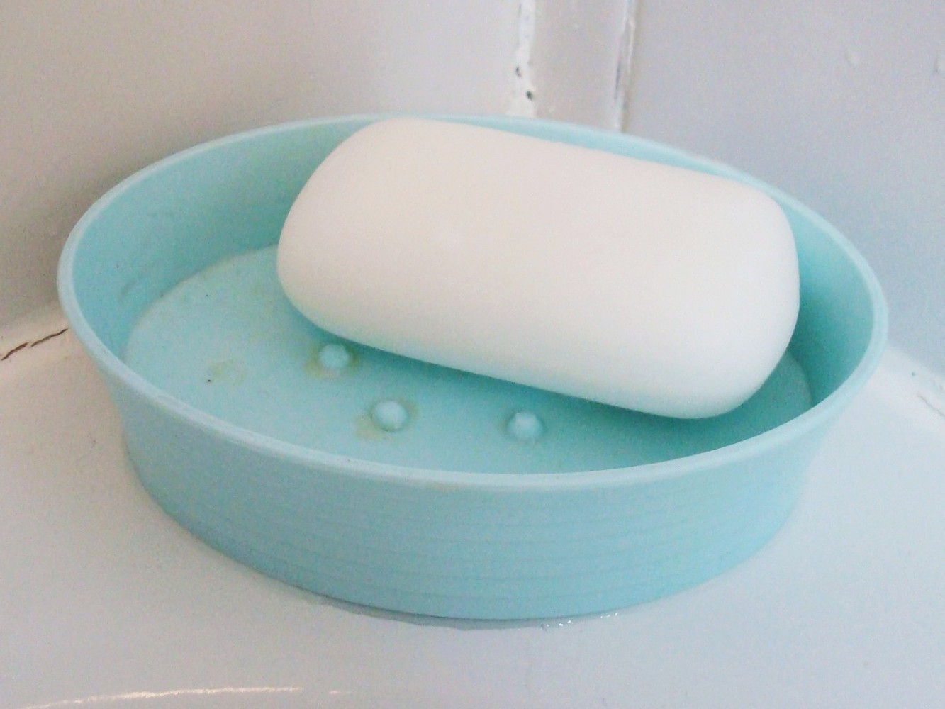 A white bar of soap in a light blue plastic soap dish.