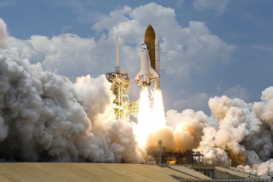 A rocket, with space shuttle attached, blasting off from Earth