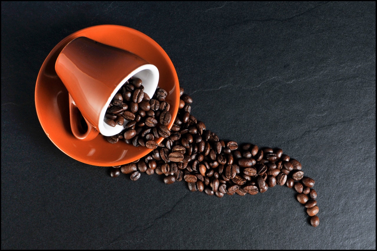 A cup on its side, with coffee beans spilling out of it