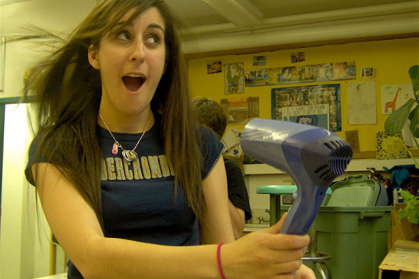 Long-haired woman posing with a blowing hairdryer.