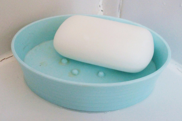 A white bar of soap in a light blue plastic soap dish.