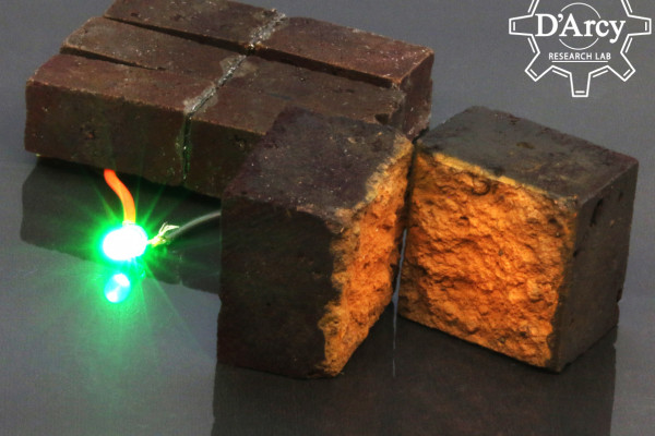 A brick, modified to store power hooked up to a glowing LED. A second brick is cut in half to show the interior