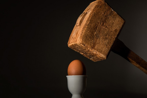 A wooden mallet about to smash an egg in a teacup