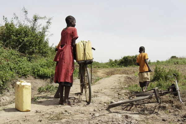 Three children walking bikes on a dirt road in Uganda.