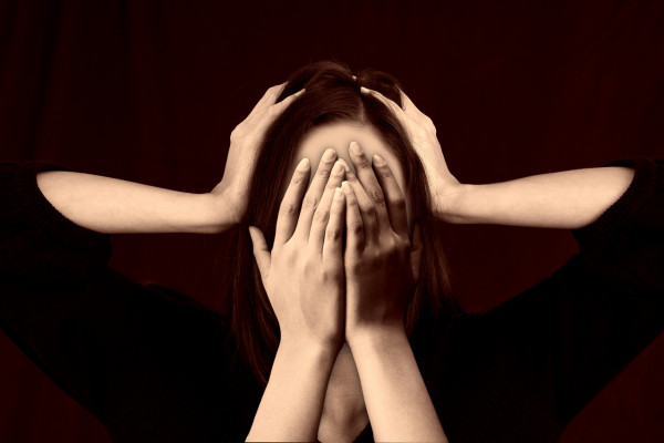 A woman clutching hear head, with another set of arms covering her face.