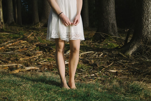 A woman in a white dress standing in a forest, shown from the waist down.