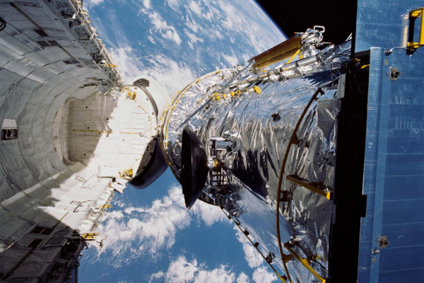 The Hubble Space Telescope is suspended above shuttle Discovery's cargo bay some 332 nautical miles above Earth