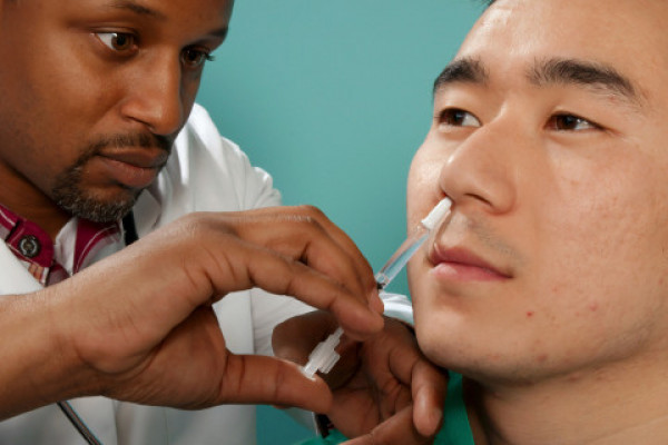 A doctor administering a vaccine up a patient's nose.