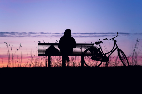 A woman sitting on a park bench watching the sunset