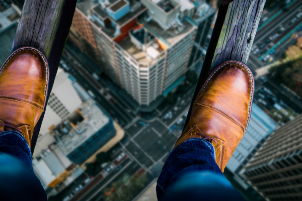 Looking down at a man's shoes as he stands on two thin wooden beams, high above a city street