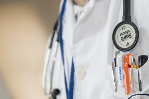 Close up of a doctor's coat, with a stethoscope and a pocket full of pens