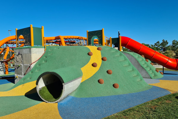 A green hill with tunnels, rock climbing and slides