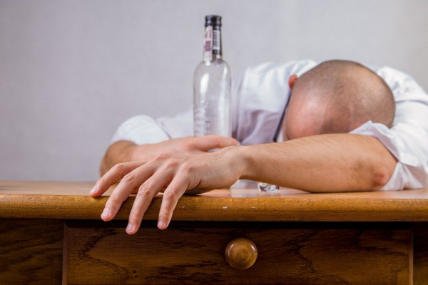 A hungover man collapsed face down on a table cradling a bottle.