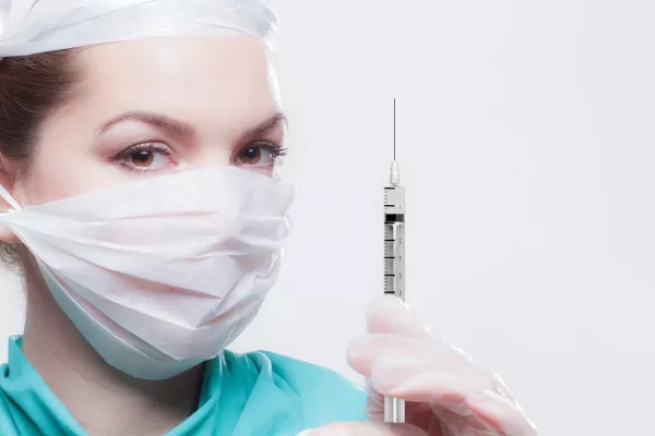 A healthcare worker wearing a mask holding a syringe.