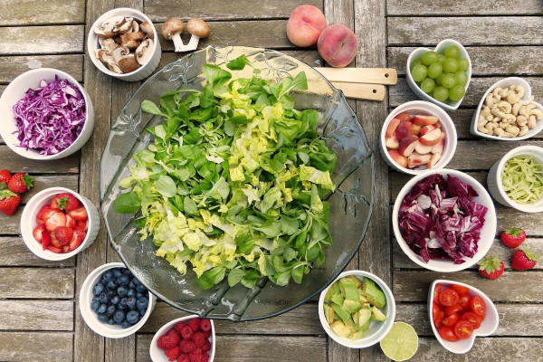 A plate of salad, surrounded by bowls of various fruits