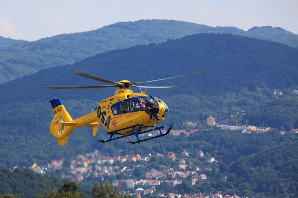 A yellow helicopter in flight above a mountainous region.