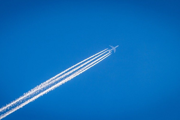 A plane flying across the sky, leaving a streaky contrail cloud behind it