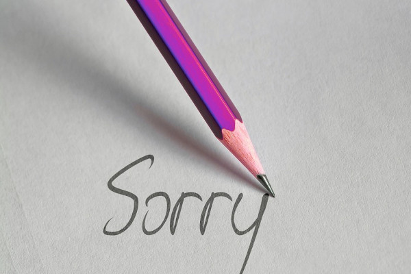 a purple pencil writing the word "sorry" on paper