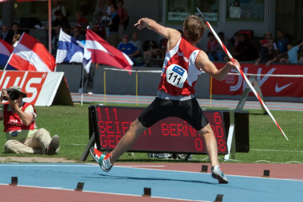 A man in a red vest pulling his arm back, ready to throw a javelin