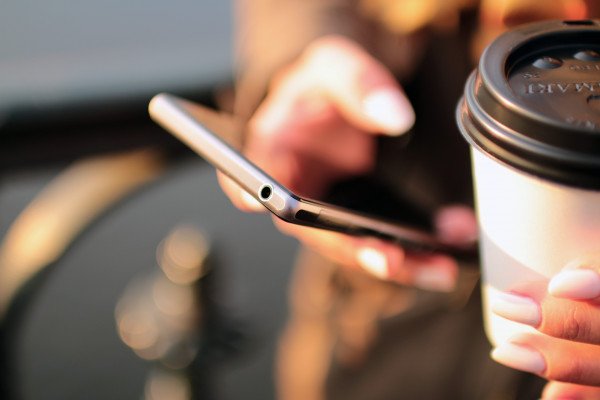 A person holding a cup of coffee while using a smartphone
