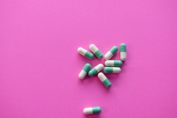 White and green pill capsules on a bright pink background