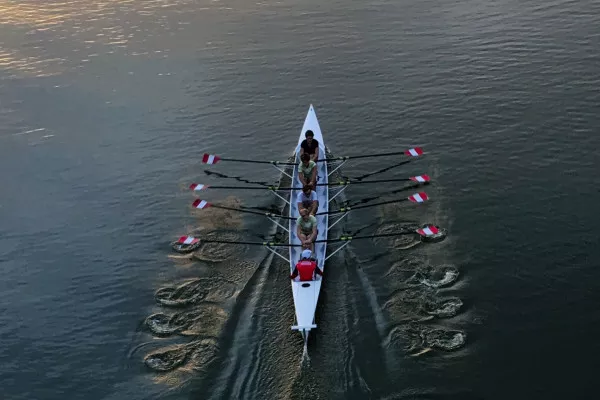 A 4 person boat rowing on water at sunset