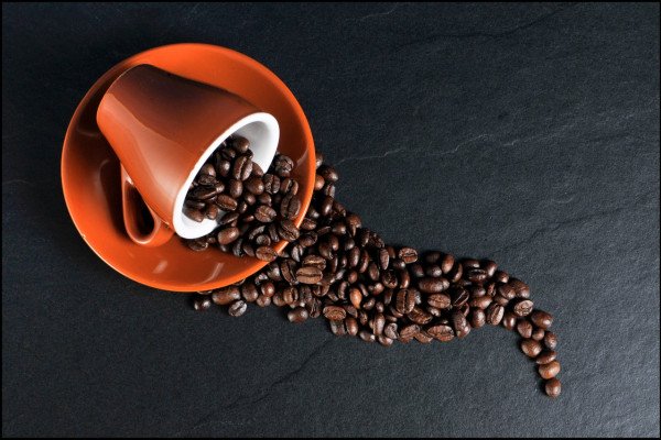 A cup on its side, with coffee beans spilling out of it