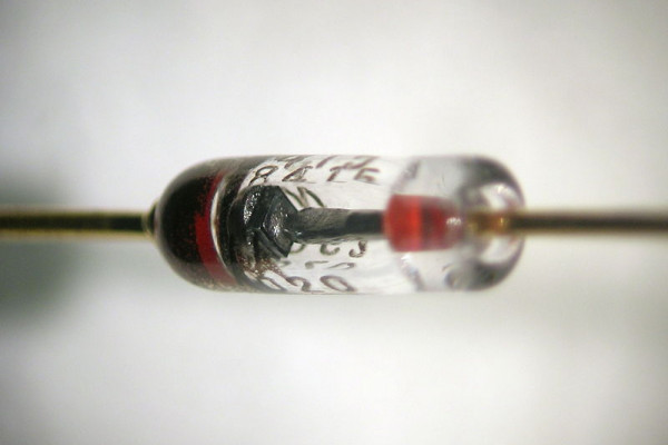 Close-up view of a silicon diode. The anode is at the right side; the cathode is at the left side (where it is marked with a black band). A square silicon crystal can be seen between the two leads.