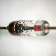 Close-up view of a silicon diode. The anode is at the right side; the cathode is at the left side (where it is marked with a black band). A square silicon crystal can be seen between the two leads.