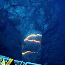  Bands of glowing magma, about 2,200 degrees Fahrenheit, are exposed as a pillow lava tube extrudes down slope from a submarine volcano. The image shows an approximately three-foot section across in an eruptive area spanning 100 yards and which runs...