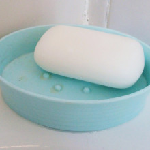 A white bar of soap in a light blue plastic soap dish.