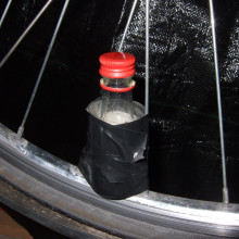The bottle is attached, by making a card tube that it just fits inside and taping it between the spokes