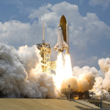 A rocket, with space shuttle attached, blasting off from Earth