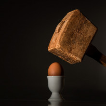 A wooden mallet about to smash an egg in a teacup