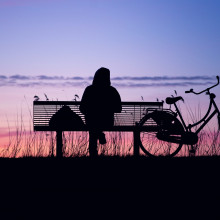 A woman sitting on a park bench watching the sunset