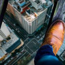 Looking down at a man's shoes as he stands on two thin wooden beams, high above a city street