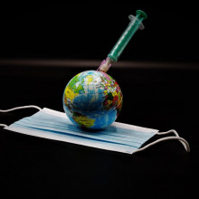 A globe lying on a facemask with a syringe stuck into it.