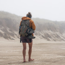 A woman with a rucksack walking on a beach