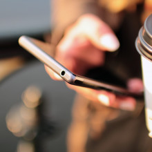 A person holding a cup of coffee while using a smartphone