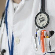 Close up of a doctor's coat, with a stethoscope and a pocket full of pens