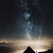 Someone shining a light up from a mountain at the stars and Milky Way.