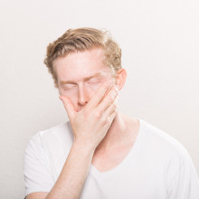 A tired man covering a yawn with his hand.