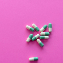 White and green pill capsules on a bright pink background