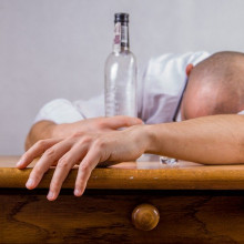 A hungover man collapsed face down on a table cradling a bottle.