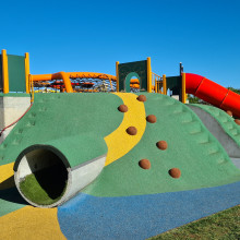 A green hill with tunnels, rock climbing and slides