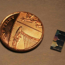 The photonic chip next to a UK penny. The chip contains micrometer and submicrometer features and guide light using a network of waveguides. The output of this network can be seen on the surface of the chip.